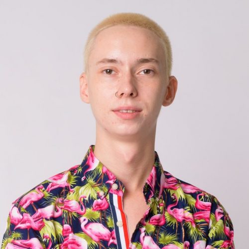 young-happy-androgynous-tourist-man-smiling-with-arms-crossed-e1629382475245.jpg